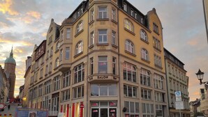 Un bâtiment d’angle avec une enseigne « Salon Bar », de nombreuses fenêtres et une autre enseigne indiquant une « Zone » réservée aux piétons.