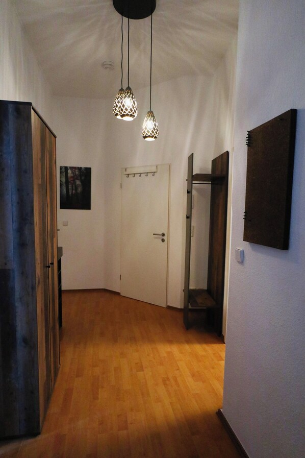 Un pasillo con suelo de madera, una puerta blanca e iluminación colgante.
