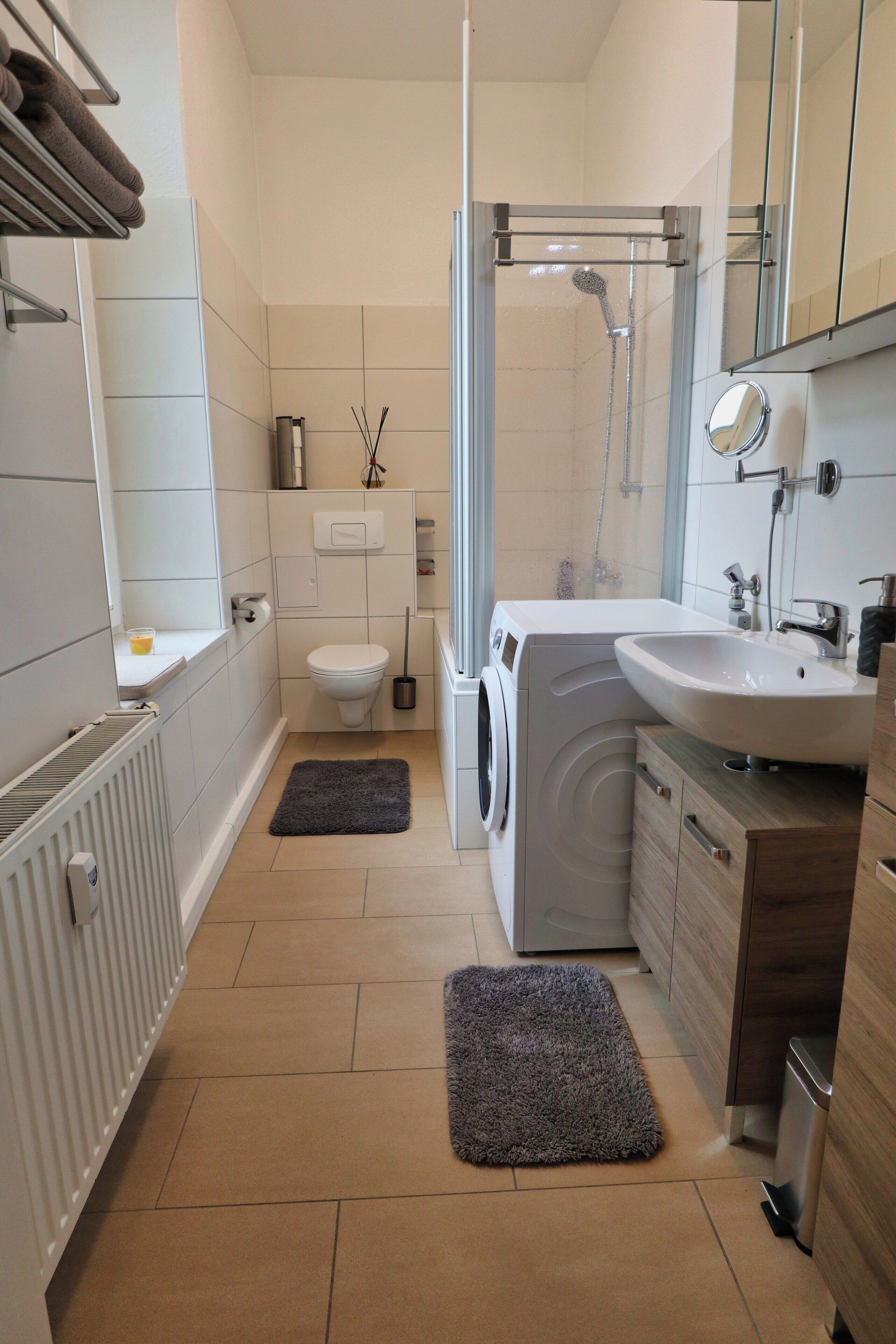 Ein modernes Badezimmer mit Toilette, Waschmaschine, Waschbecken und Dusche.