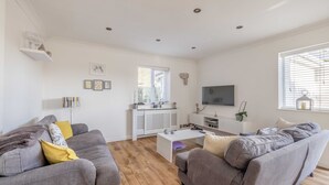 A modern living room with two grey sofas, a white coffee table, and a TV mounted on the wall. - Spacious 6 Bedroom House in Maidenhead/ Windsor (Maidenhead)