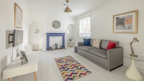 A modern living room with a grey sofa, a white desk, a colorful rug, a fireplace, and a ceiling light. - Spacious 6 Bedroom House in Maidenhead/ Windsor (Maidenhead)
