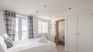 A bedroom with a large bed, a bedside table, a wardrobe, and a view of the city through the window. - Spacious 6 Bedroom House in Maidenhead/ Windsor (Maidenhead)