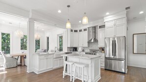 A spacious kitchen with white cabinetry, a central island with stools, stainless steel appliances, and pendant lighting. - Prime Seagrove Location | Private Pool, Bikes, Porches, Steps to Beach Access (Santa Rosa Beach)