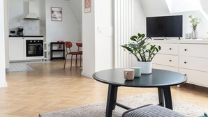 Een moderne keuken met een fornuis, oven en een eethoek met stoelen. Er staat een tv op een kast en een plant op een tafel.