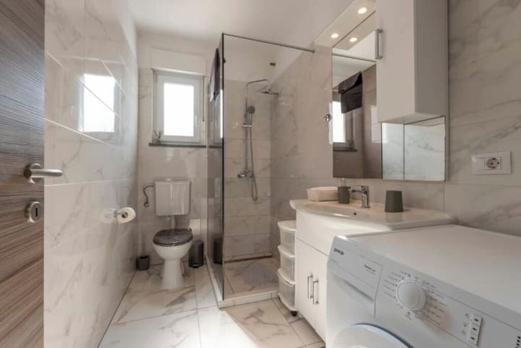 Un bagno moderno con box doccia in vetro, un water, un lavandino e una lavatrice.