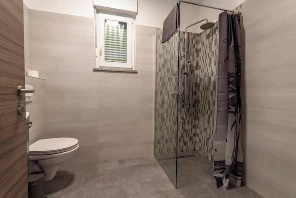 Een moderne badkamer met een toilet, een douche met glazen deur en een raam boven het toilet.
