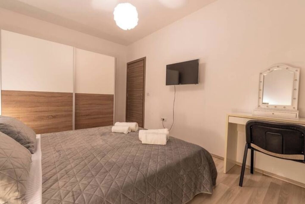 A bedroom with a bed, a desk, a chair, a TV, and a mirror.