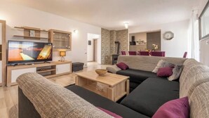 A modern living room with a large flat-screen TV, a dark-colored sofa, a wooden coffee table, and a stone accent wall. - Holiday home Galižana (Galižana)