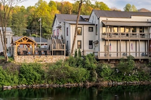 A waterfront property with a stone patio, outdoor seating, and a large building with multiple windows and balconies.