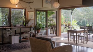 Amplia sala de estar con cocina, comedor y ventanas grandes que ofrecen vistas al exterior.