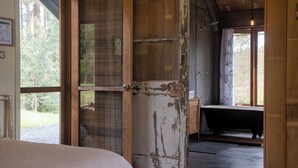 Una habitación rústica de madera con un gran ventanal abierto, una ventana con vistas a la vegetación y una bañera.