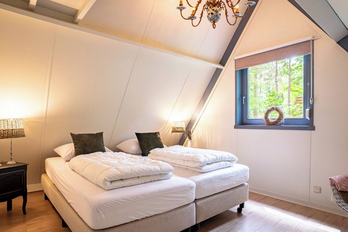 A bedroom with two beds, a chandelier, a window with a wreath, and a nightstand with a lamp.