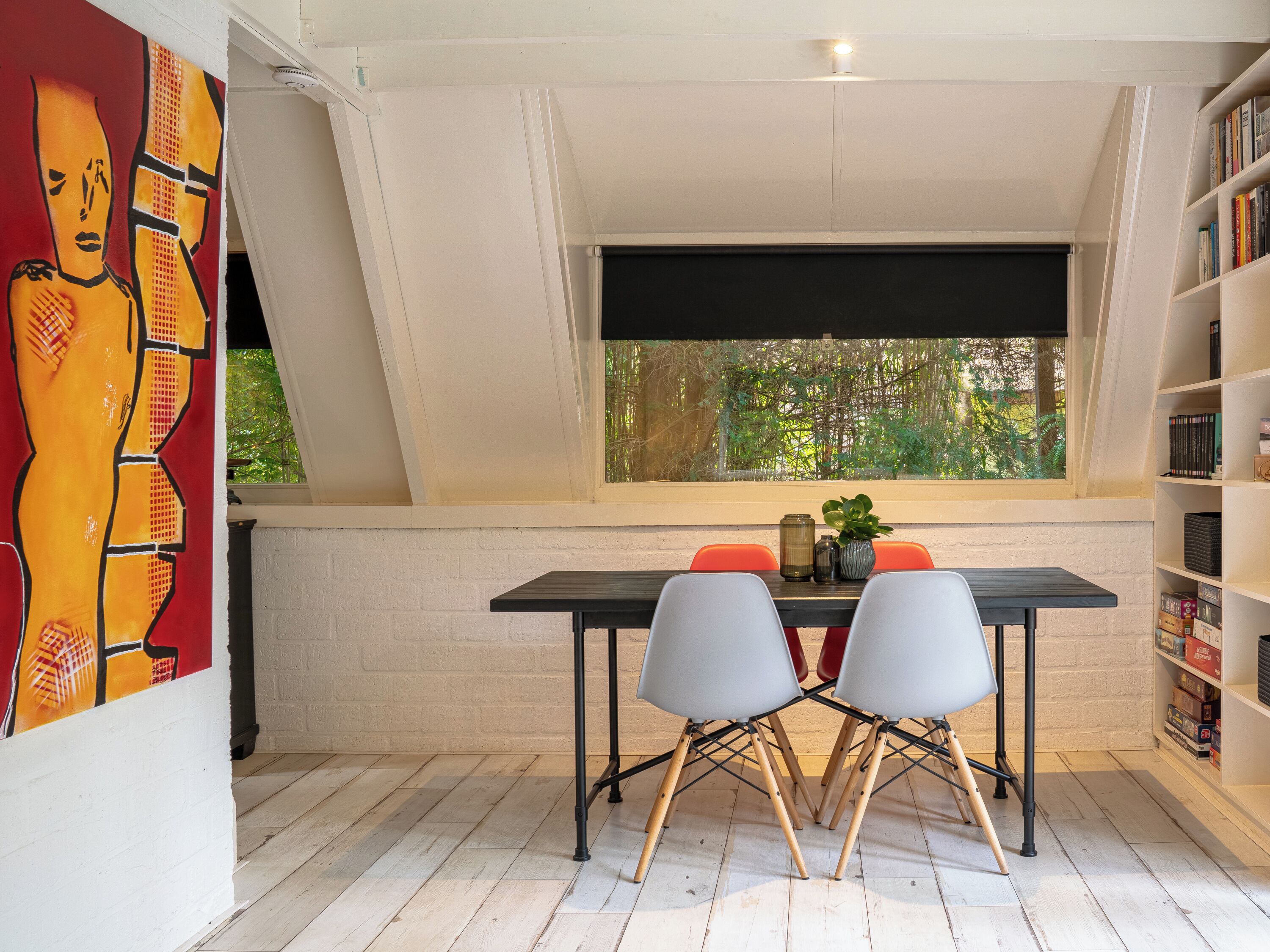 Un comedor con mesa y sillas, una estantería y un ventanal con vistas a zonas verdes.