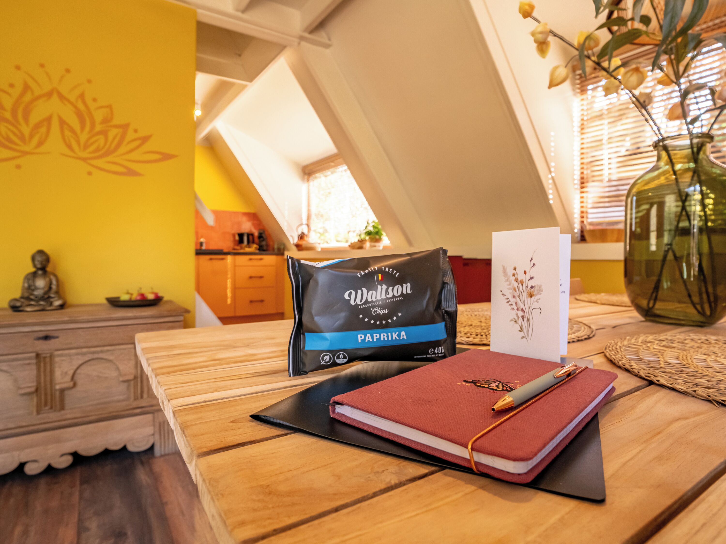 A wooden table with a notebook, a bag of chips, and a card.