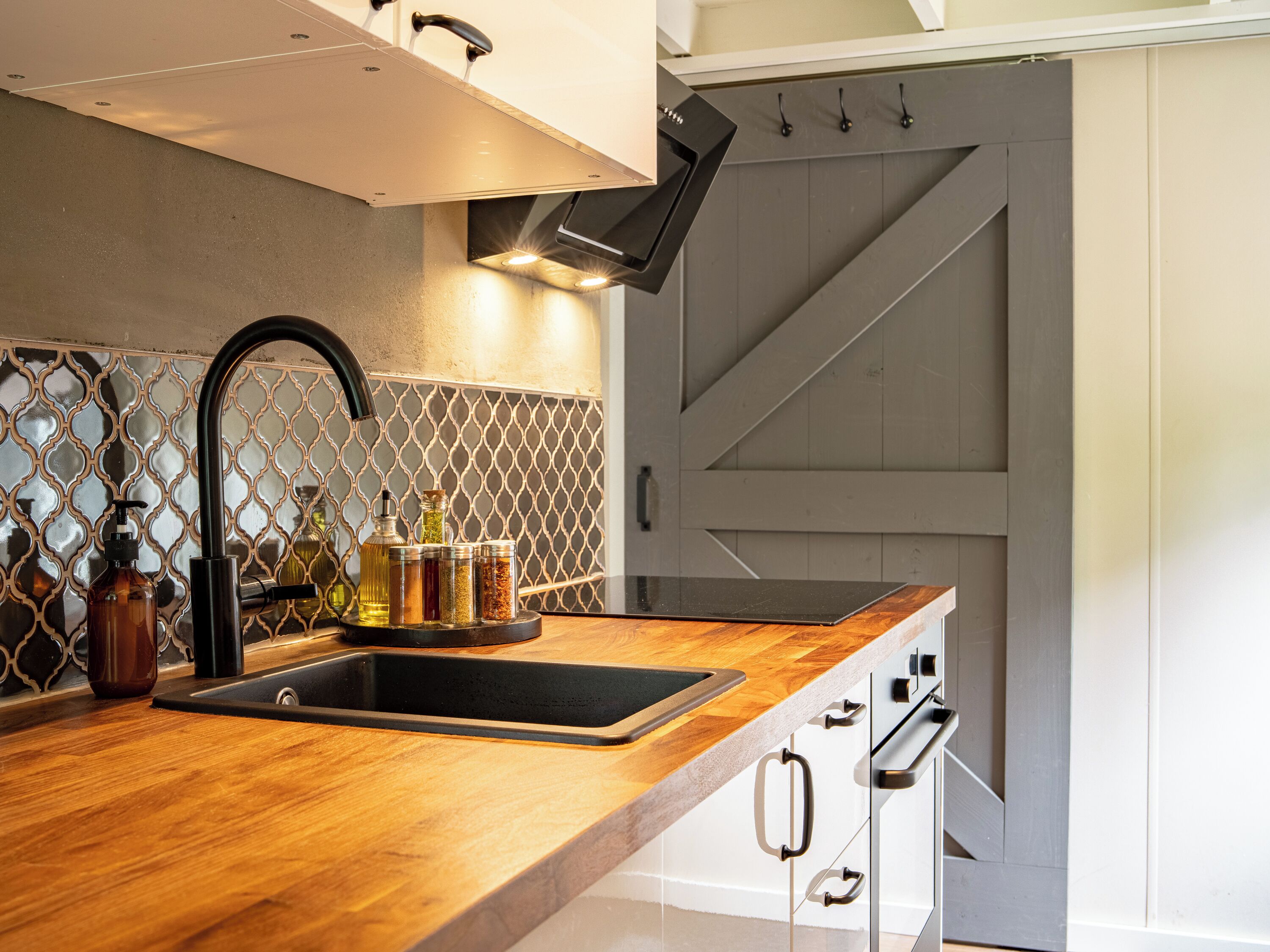 A modern kitchen with a wooden countertop, a black faucet, and a stainless steel sink. There are various bottles and containers on the counter.