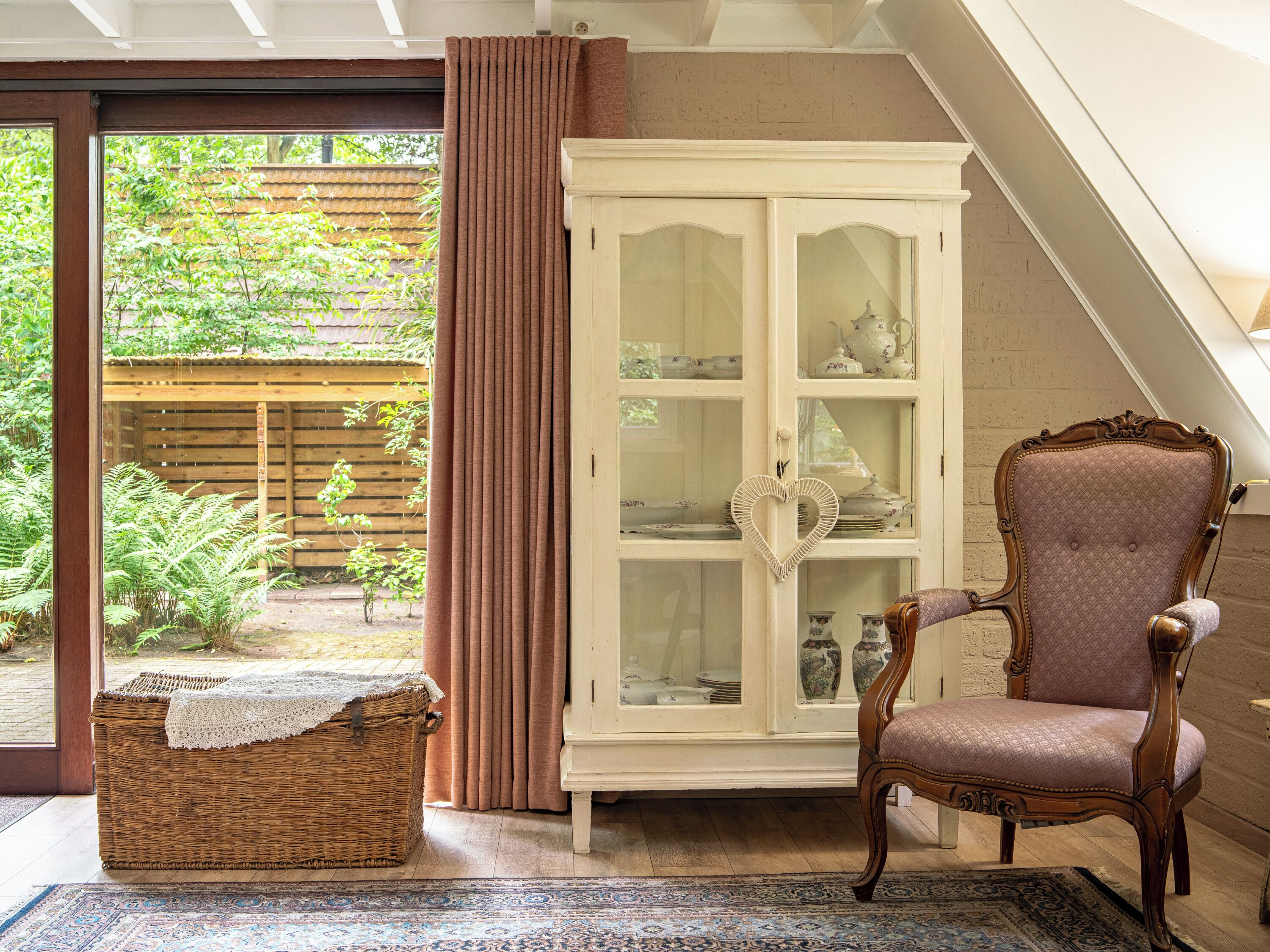 A room with a wicker bench, a cabinet with glass doors, and a chair.