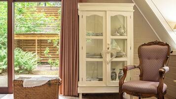 A room with a wicker bench, a cabinet with glass doors, and a chair.
