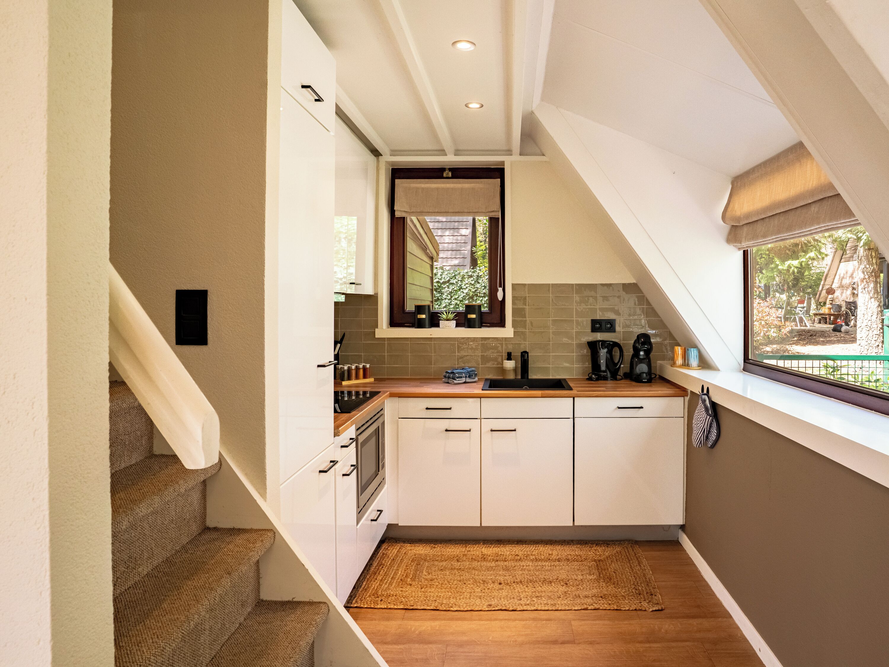 A compact kitchen with white cabinets, a wooden countertop, and a window with a view of the outdoors.
