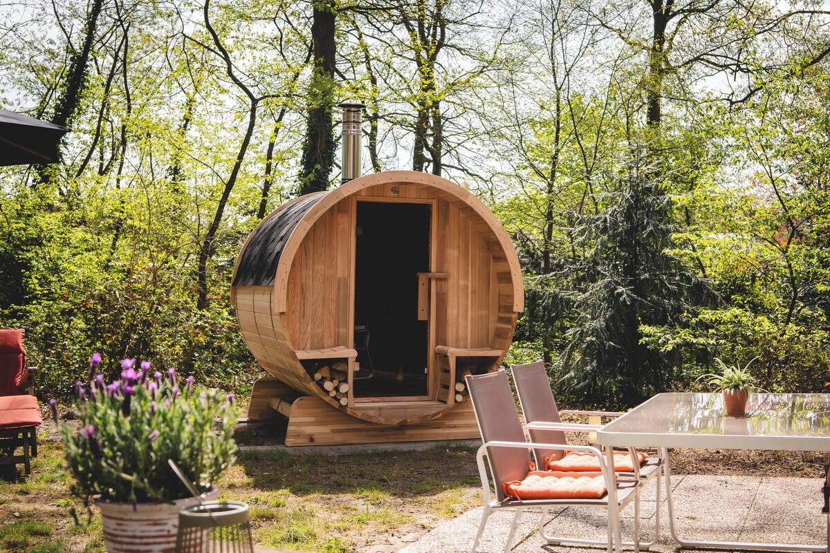 A wooden sauna in a forest setting with a table and chairs nearby.
