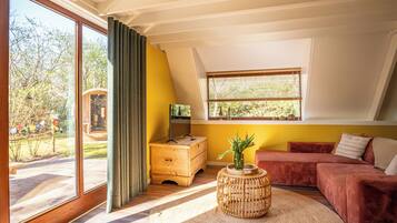 A modern living room with a large sliding glass door, a wooden bench outside, a red sofa, a small wooden table, and a window with blinds.