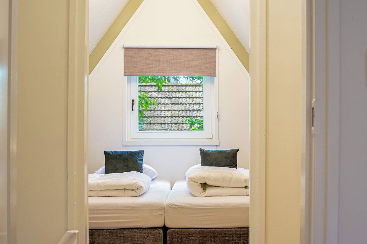 A bedroom with two beds, a window with a view of greenery, and a sloped ceiling.