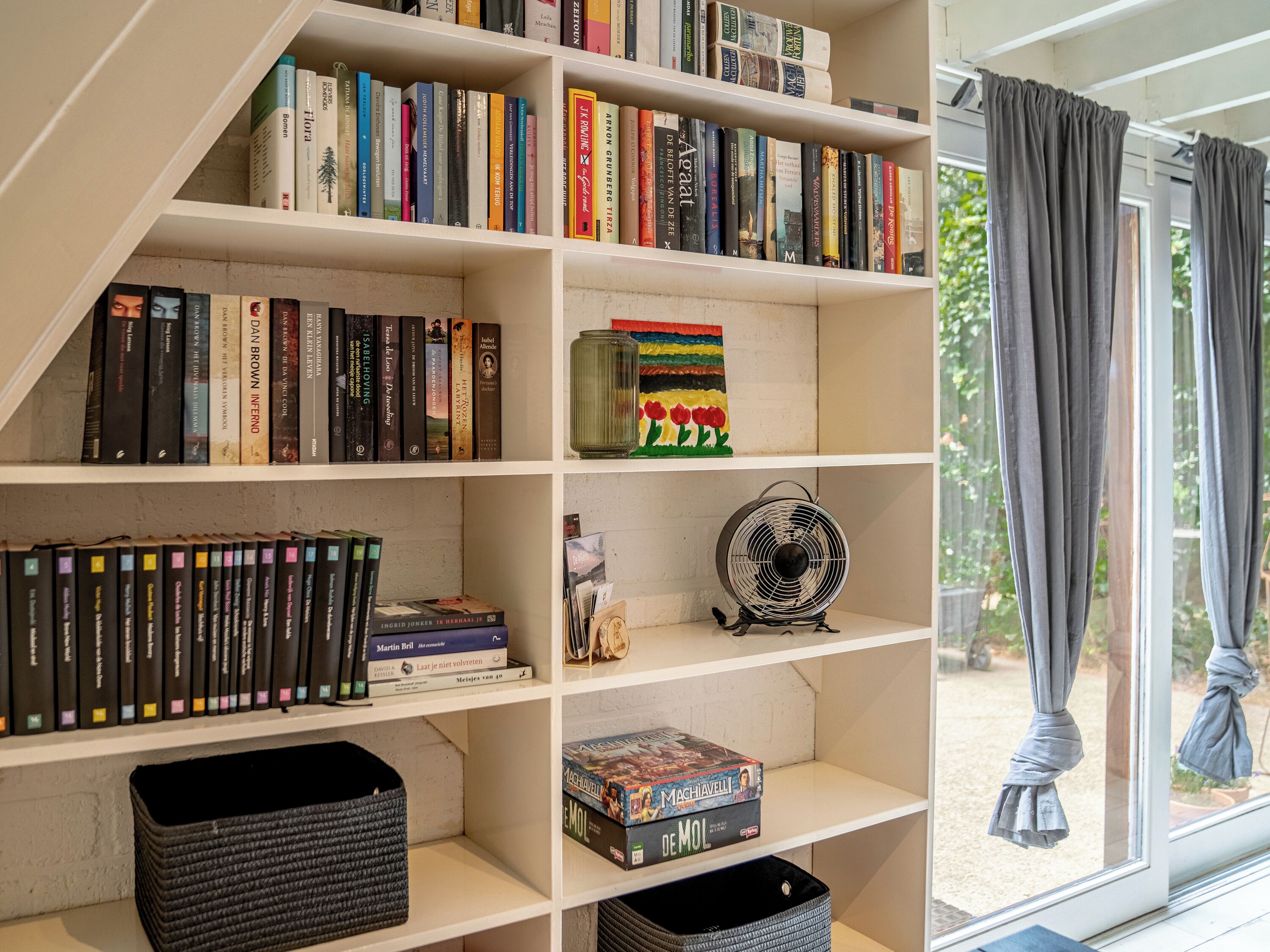 A bookshelf with various books and a fan.
