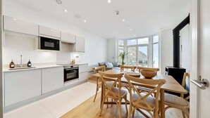 A modern kitchen with white cabinetry, a dining area with wooden chairs, and a large window providing natural light.