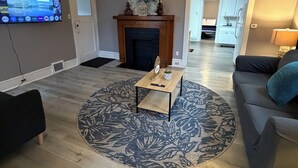 Un salon avec une cheminée, un téléviseur fixé au mur et une table basse ronde.