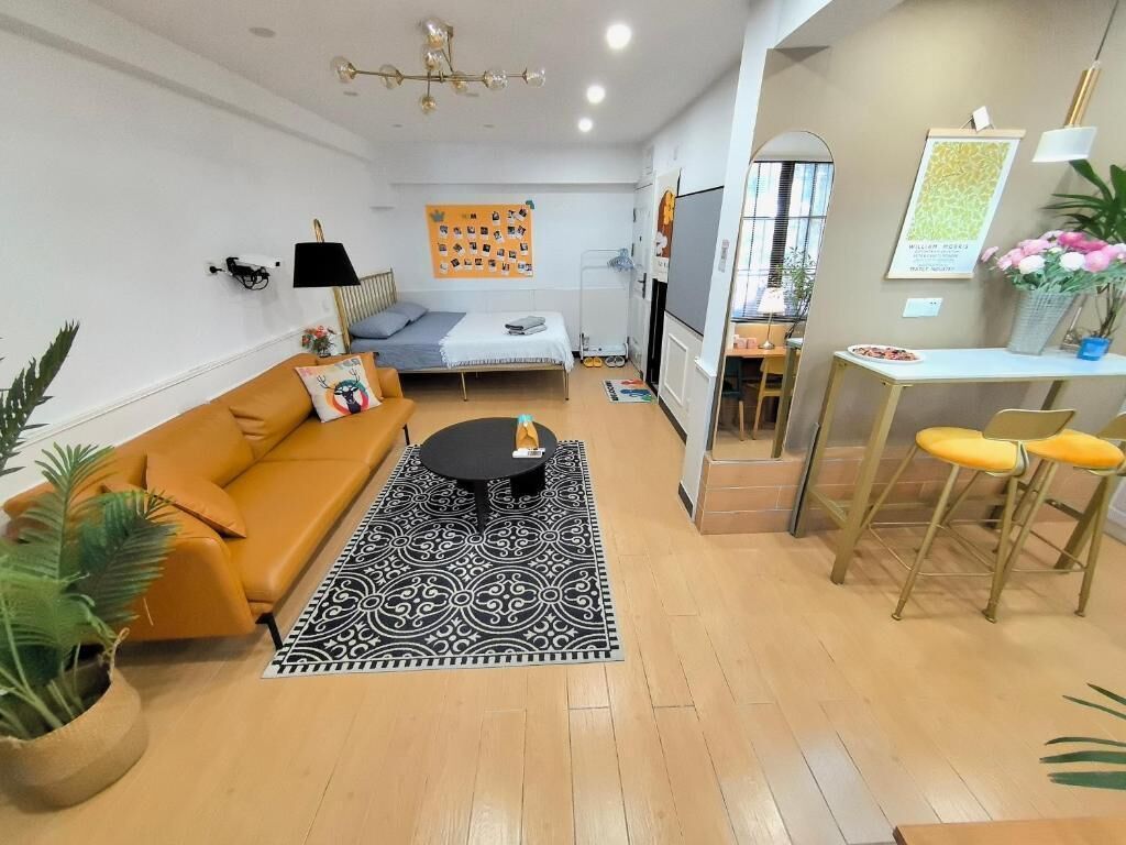 Ein modernes Wohnzimmer mit Sofa, Couchtisch, einem gemusterten Teppich, einem Essbereich mit Tisch und Stühlen sowie einem Bett mit blauer Kopfteil.
