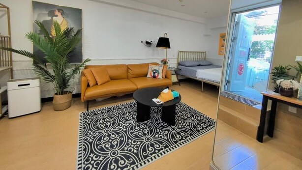 A modern living room with a sofa, coffee table, and a patterned rug. There is a bed with a headboard and a small table with a lamp. - Shanghai Hills&Zinn Changle road Homestay (Shanghai)