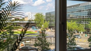 A view from inside a building looking out at a modern urban street with glass buildings, a bus stop, and parked cars. - Cosy Stay in a Two Bed Flat (Milton Keynes)