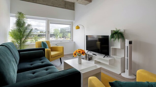 A modern living room with a sofa, armchair, TV, and a potted plant. - Cosy Stay in a Two Bed Flat (Milton Keynes)