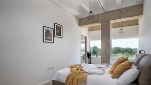 A modern bedroom with a large bed, a view of greenery outside, and a concrete ceiling. - The Yellow Corporate Suite (Milton Keynes)