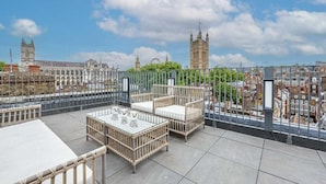 Een terras op het dak met rieten meubels, een glazen tafel en uitzicht op de Big Ben klokkentoren.