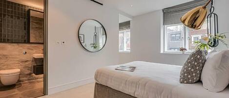 A modern bedroom with a bed, a round mirror, and a window with a view.