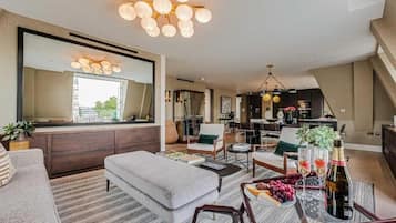Uma sala de estar moderna com um espelho grande, uma área de jantar e uma cozinha ao fundo.
