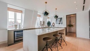 Een moderne keuken met een centraal eiland, barkrukken, hanglampen en uitzicht op de stad.