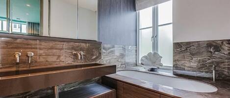A modern bathroom with a large mirror, a marble countertop, and a window with a view.