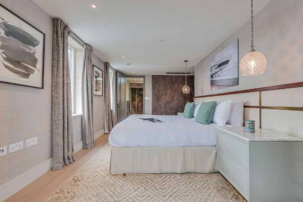 Une chambre moderne avec un grand lit, une table de chevet, un luminaire suspendu et une vue sur une autre pièce.