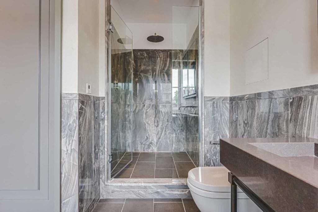 Une salle de bain moderne avec une douche en verre, un mur recouvert de carreaux de marbre et des toilettes de couleur beige.
