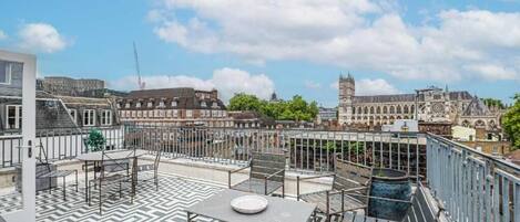 A rooftop terrace with a chevron-patterned floor, outdoor seating, and a view of historic buildings including a tower.
