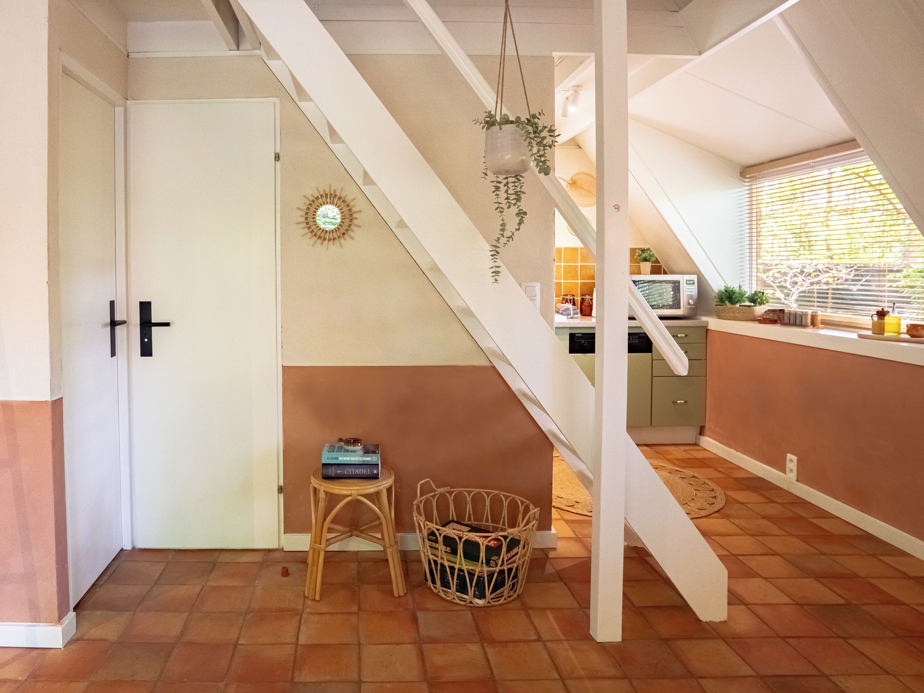 Una cocina con una escalera blanca, una cesta de mimbre y una puerta con pomo negro.