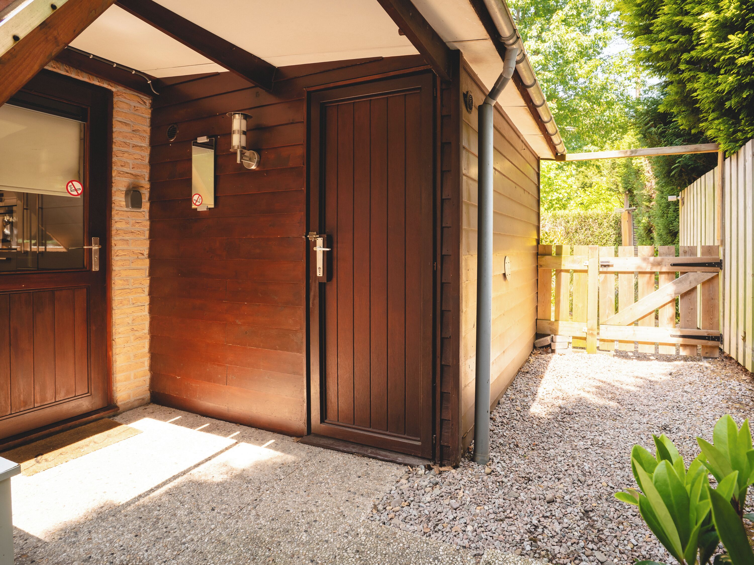 A wooden building with a large door and a window, gravel ground, and a wooden fence.