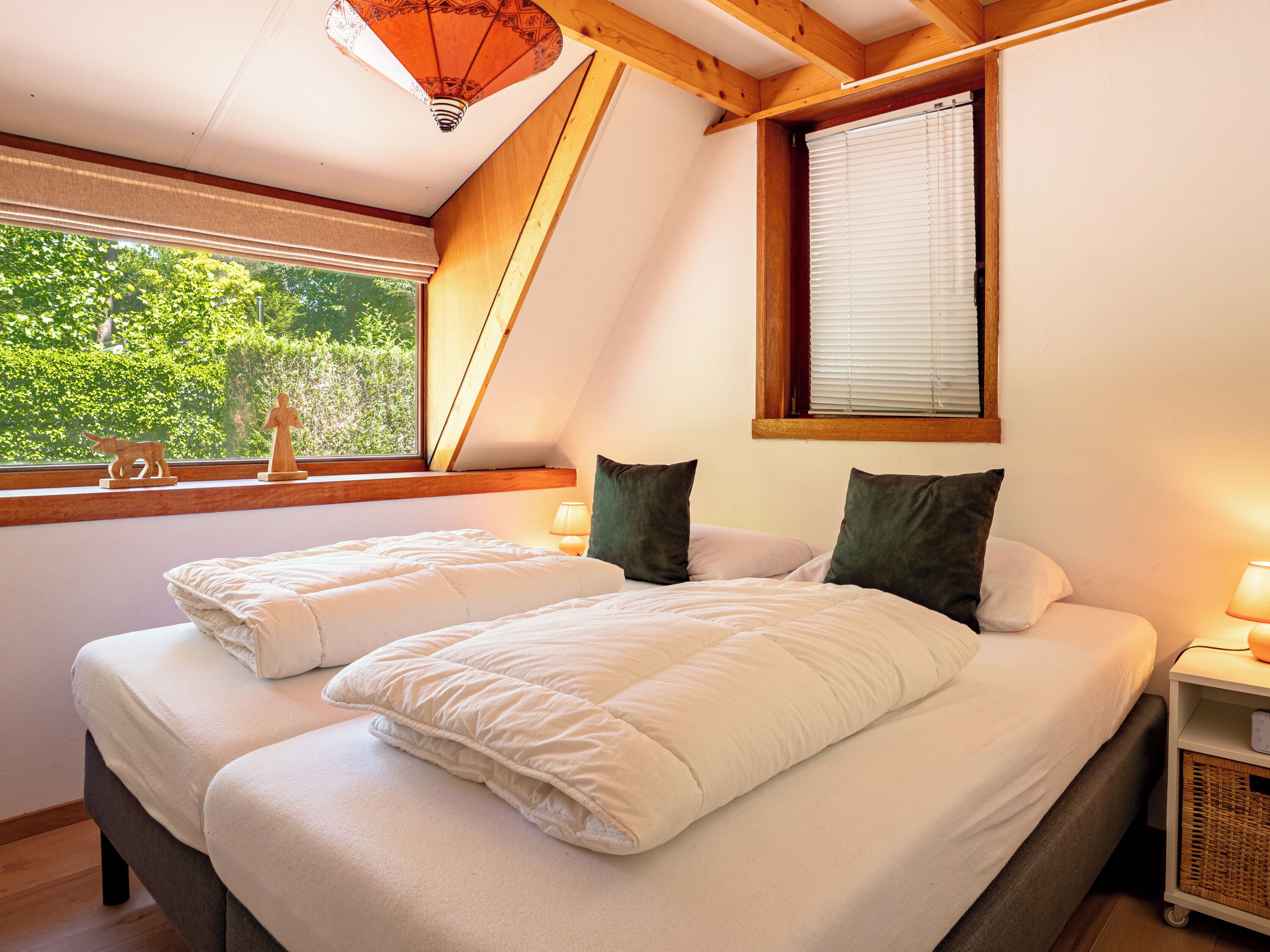 Un dormitorio con dos camas, una ventana que ofrece vistas a zonas verdes, una lámpara en la mesita de noche y un techo de madera.