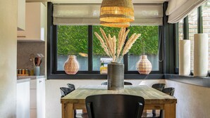 A dining area with a wooden table, black chairs, a hanging light fixture, and large windows with views of greenery. - Boshuisje Rekem Three-Bedroom Houses (Lanaken)