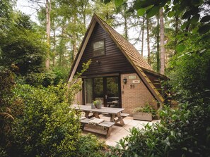 A small, rustic cabin with a wooden exterior, a large sliding glass door, and a picnic table in front. - Boshuisje Rekem Three-Bedroom Houses (Lanaken)