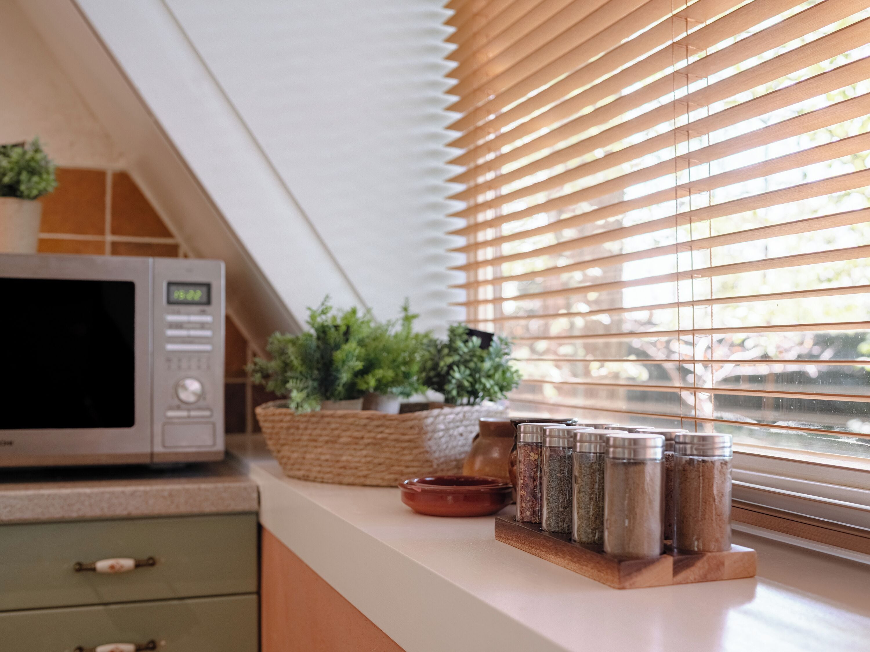 Una cocina con microondas, especiero y plantas en macetas sobre la encimera.