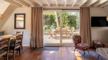 Ein geräumiges Zimmer mit Essbereich, einer gemütlichen Sitzecke mit Sofa und Sessel sowie einer großen Glasschiebetür, die auf eine Außenpatio führt.