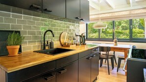 A modern kitchen with a brick backsplash, black cabinets, and a wooden countertop. - Boshuisje Rekem Three-Bedroom Houses (Lanaken)