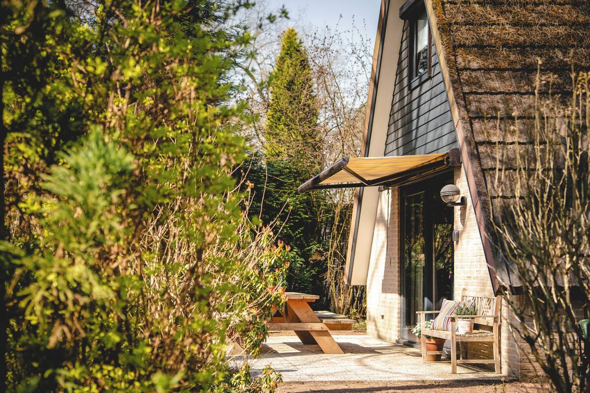 A patio area with a wooden table and chairs, a brick wall, and a window overlooking a garden.
